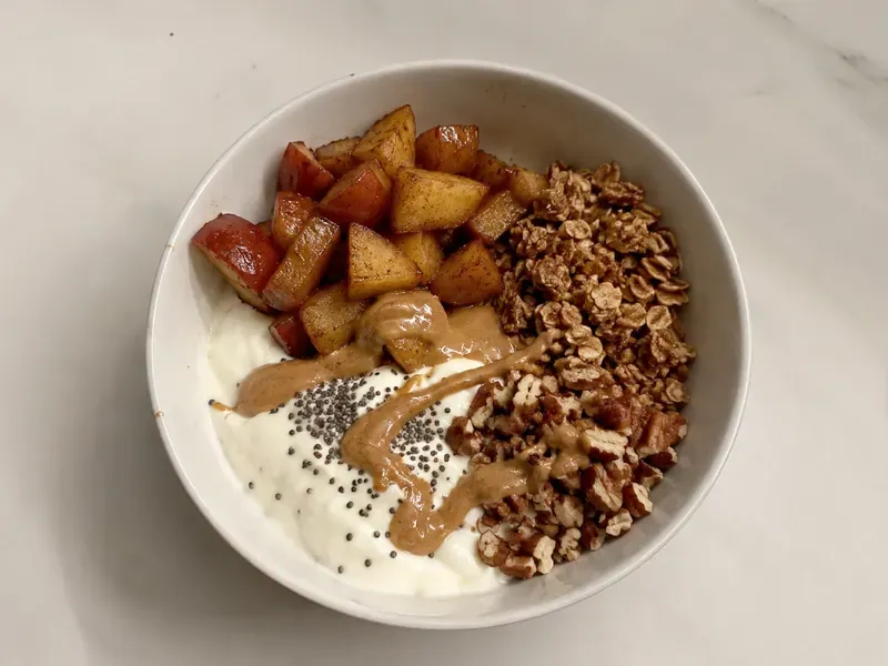 Apple cinnamon protein yogurt bowl with warm cinnamon apples, granola, nuts, and a creamy Greek yogurt base.