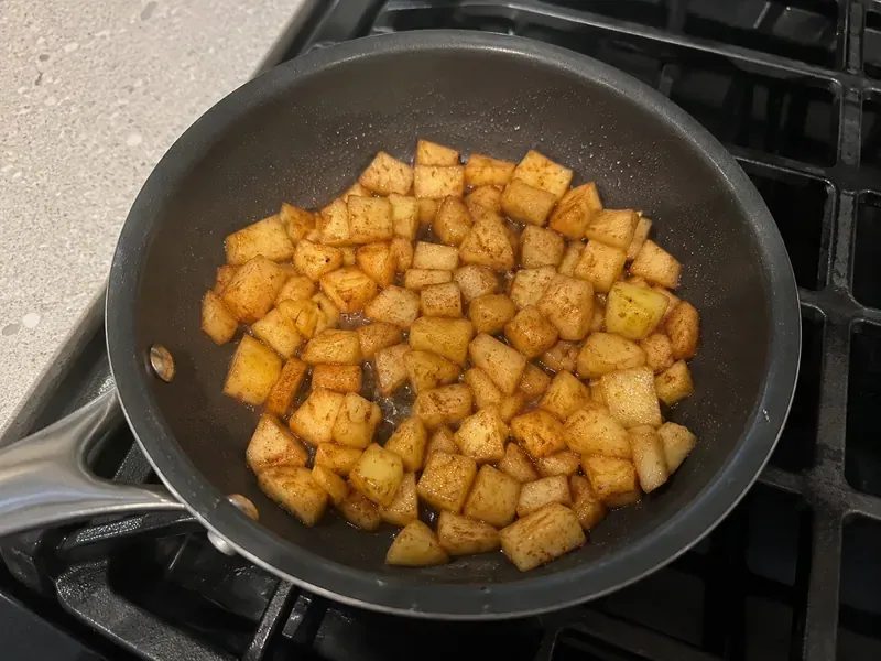 Diced apples cooking with cinnamon in a small skillet.