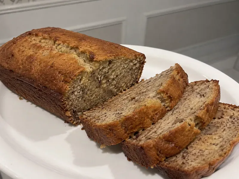 Banana Bread Recipe with Yogurt sliced on a board with a golden crust and moist tender crumb.