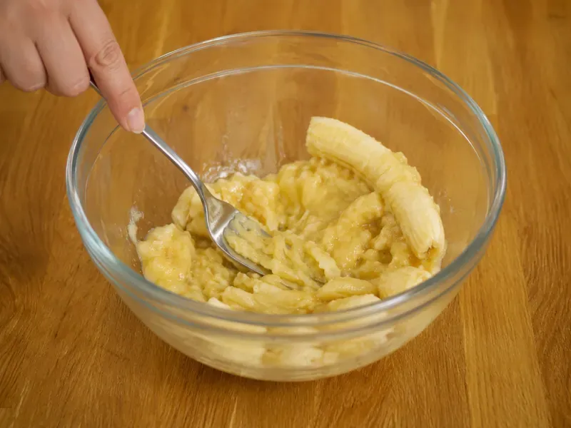 Ripe bananas mashed with a fork in a mixing bowl.