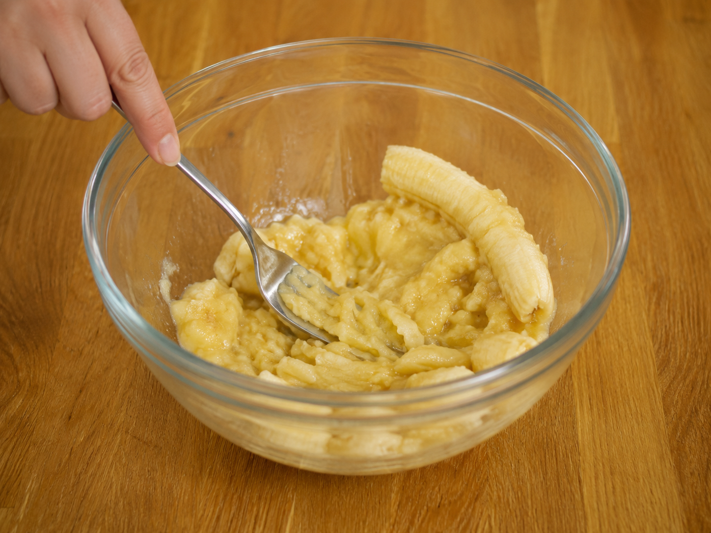 Ripe bananas mashed with a fork in a mixing bowl.