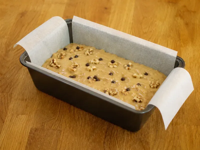 Banana bread batter spread into a lined loaf pan before baking.
