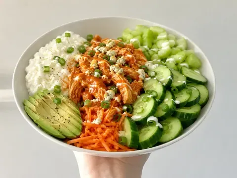 Buffalo chicken cottage cheese bowl with cucumber, carrots, celery, avocado, green onions, and buffalo sauce.