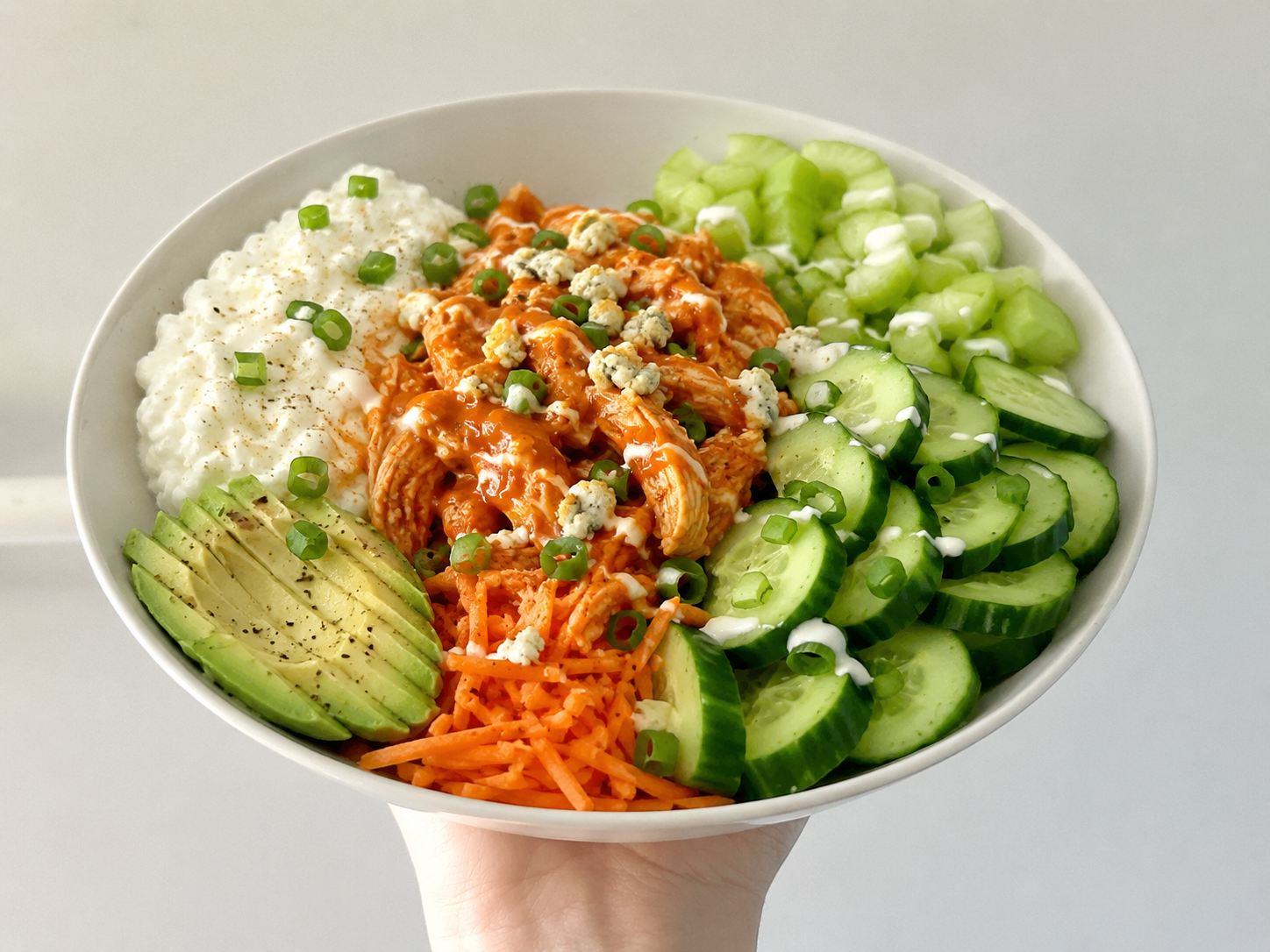 Buffalo chicken cottage cheese bowl with cucumber, carrots, celery, avocado, green onions, and buffalo sauce.