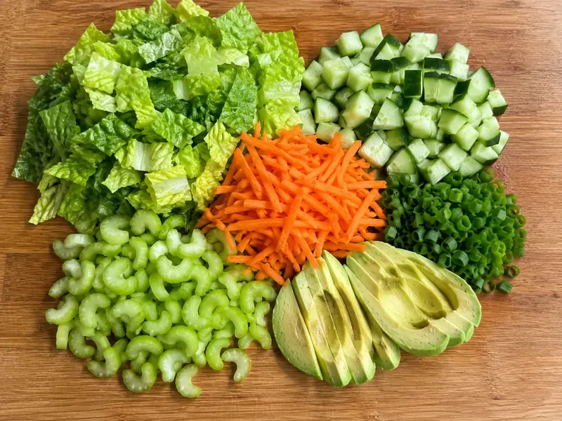 Romaine, cucumber, carrots, celery, avocado, and green onions prepared for buffalo chicken cottage cheese bowls.