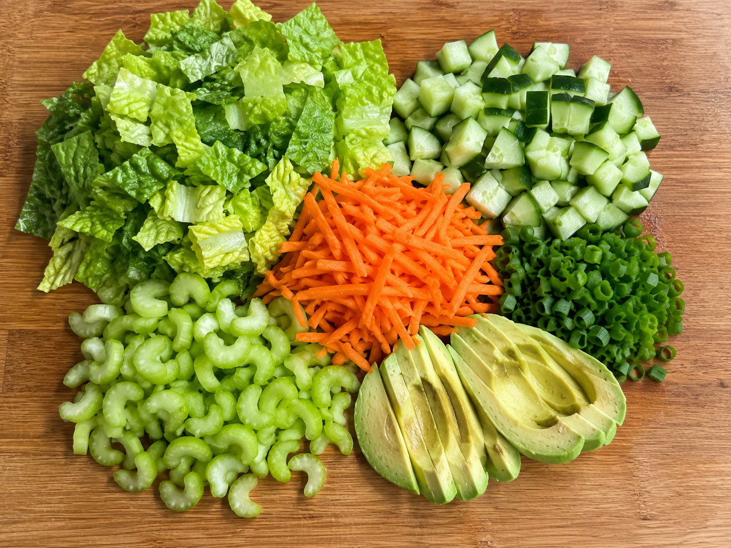 Romaine, cucumber, carrots, celery, avocado, and green onions prepared for buffalo chicken cottage cheese bowls.