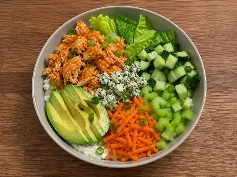 Buffalo chicken, romaine, cucumber, carrots, celery, avocado, and green onions added to a cottage cheese bowl.