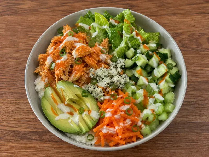 Finished buffalo chicken cottage cheese bowls with vegetables, avocado, green onions, buffalo sauce, and cottage cheese.