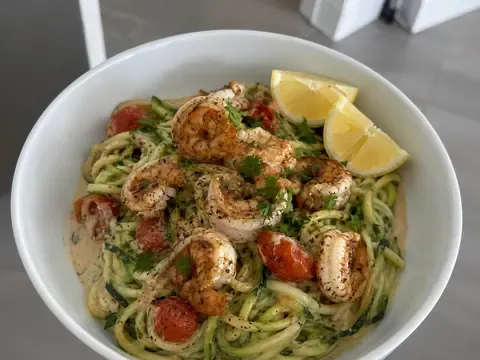 Cajun shrimp zucchini noodle bowl with seasoned shrimp, zucchini noodles, cherry tomatoes, creamy sauce, parsley, and lemon.
