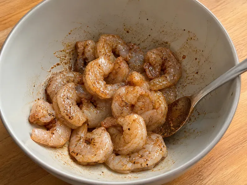 Raw shrimp tossed with Cajun seasoning in a bowl.