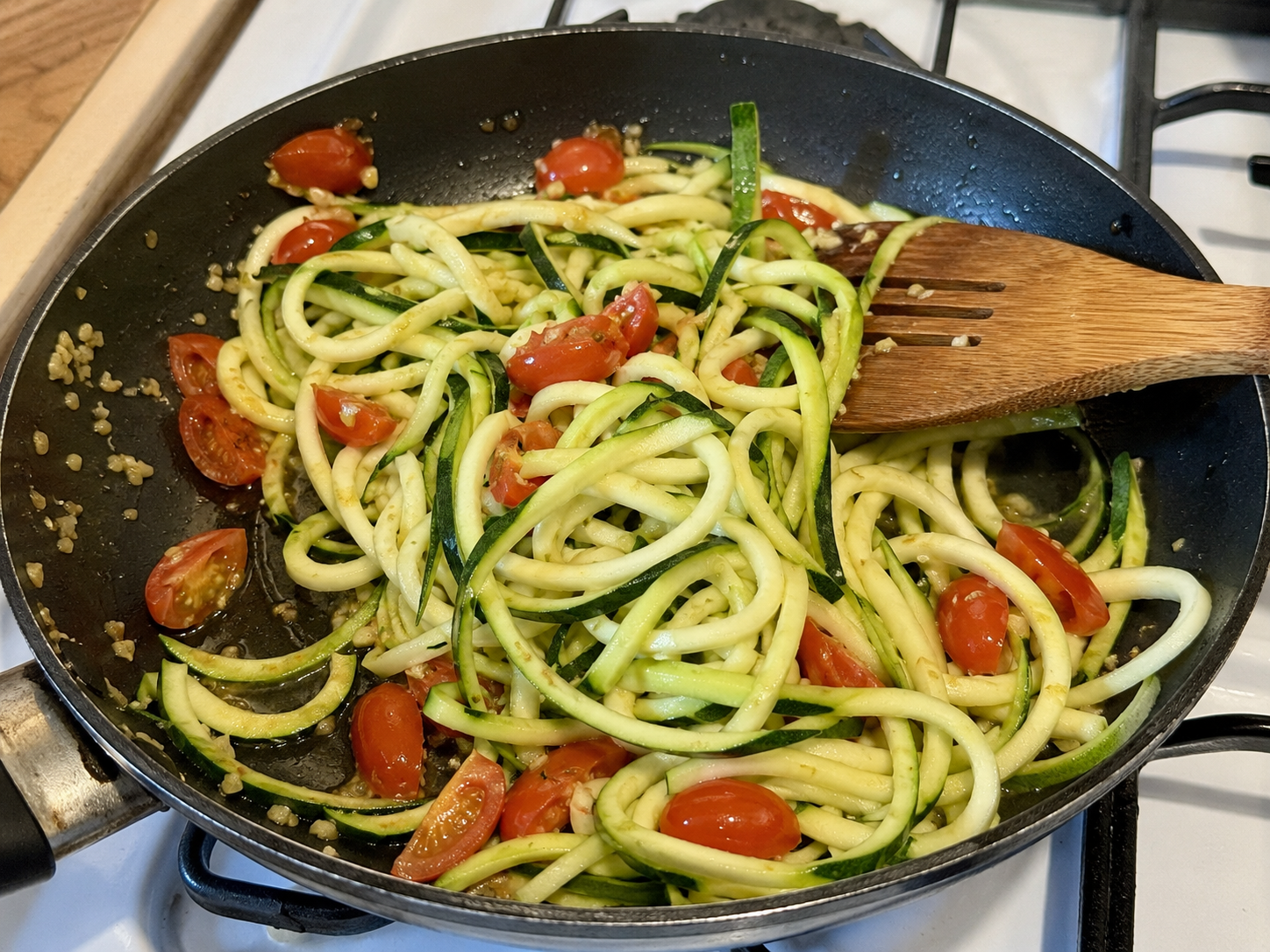 Zucchini noodles cooking with garlic and cherry tomatoes in a skillet.