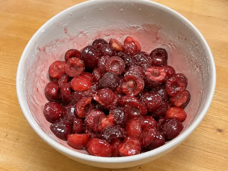 Cherries mixed with sugar, cornstarch, lemon juice, vanilla, and salt in a bowl.