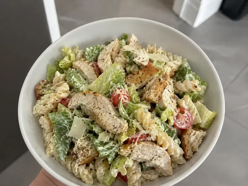 Chicken Caesar pasta salad with seasoned chicken, short pasta, romaine, parmesan, and creamy Caesar dressing.