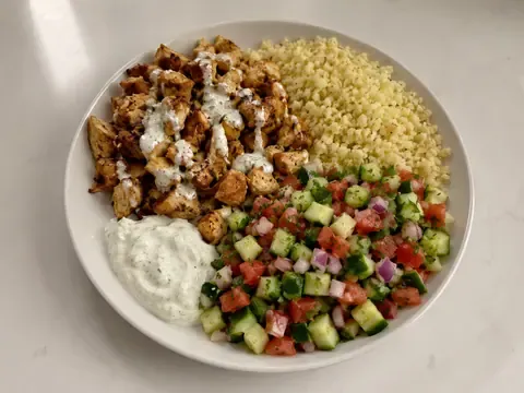 Chicken shawarma protein bowl with spiced chicken, cauliflower rice, cucumber tomato salad, parsley, and garlic yogurt sauce.