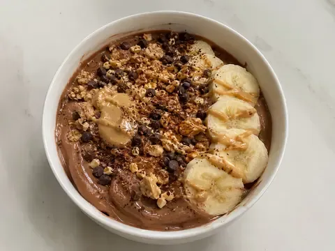 Chocolate peanut butter protein yogurt bowl with banana slices, chocolate chips, chopped peanuts, granola, and peanut butter drizzle.