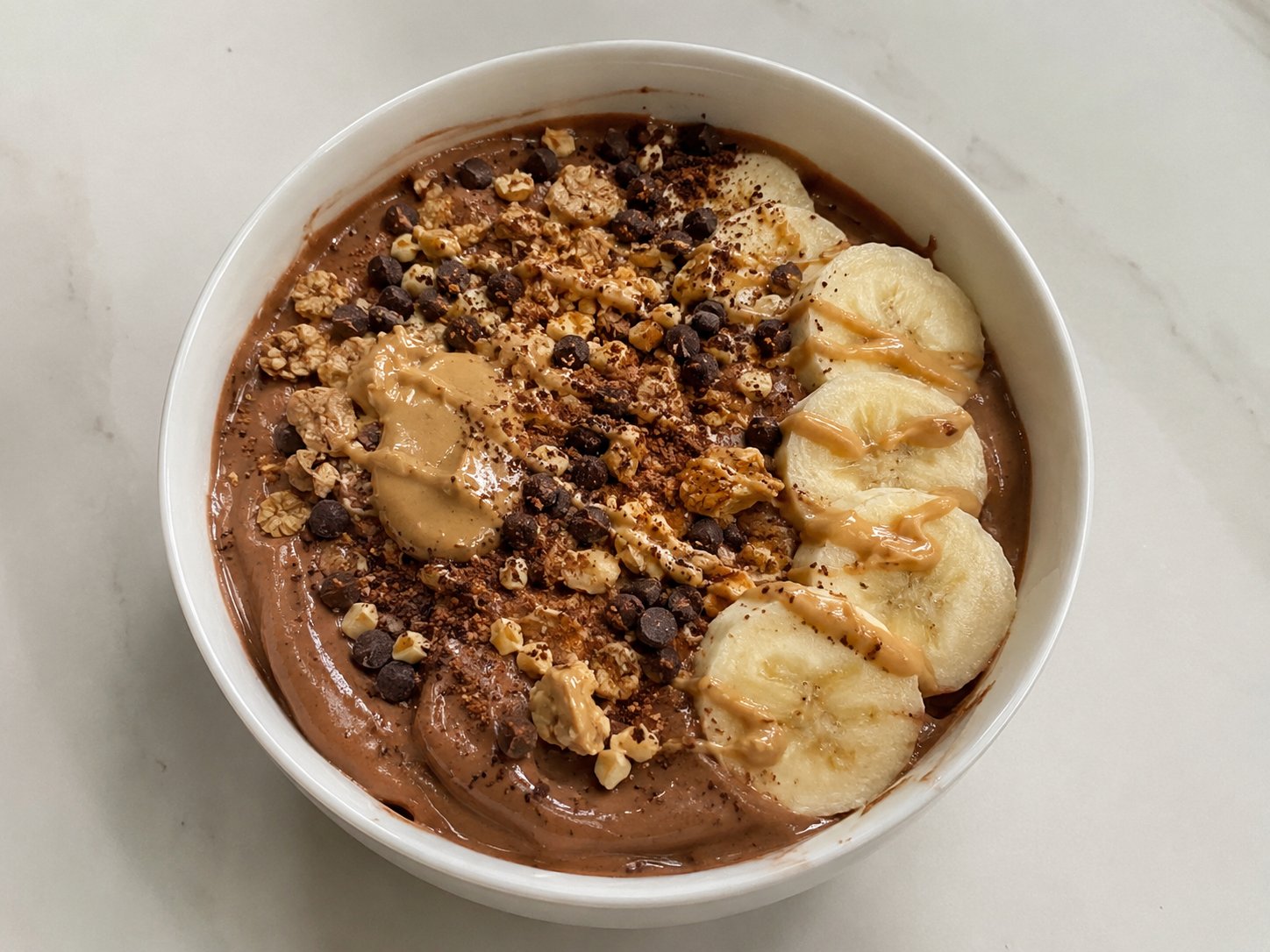 Chocolate peanut butter protein yogurt bowl with banana slices, chocolate chips, chopped peanuts, granola, and peanut butter drizzle.