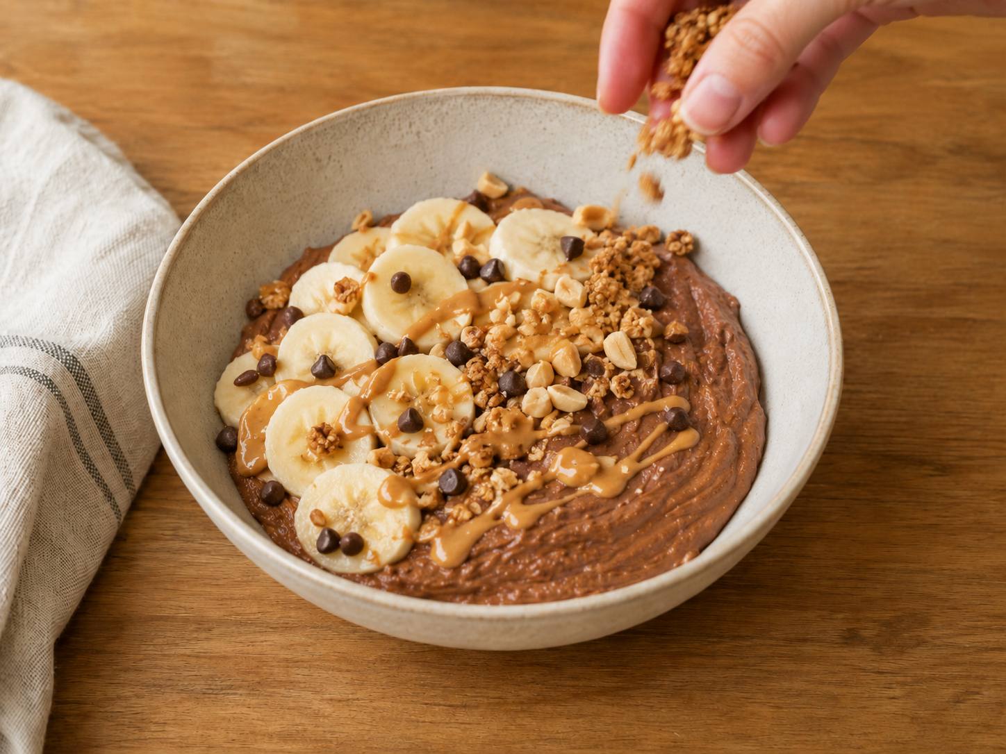 Chocolate protein yogurt bowl topped with banana, chocolate chips, chopped peanuts, granola, and peanut butter drizzle.