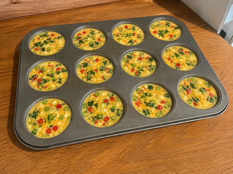 Egg bite mixture with vegetables and cheese divided into a muffin tin before baking.
