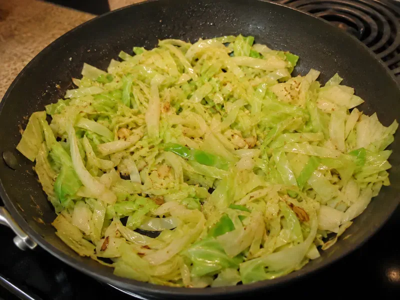 Sliced cabbage and garlic cooking in a skillet until softened.