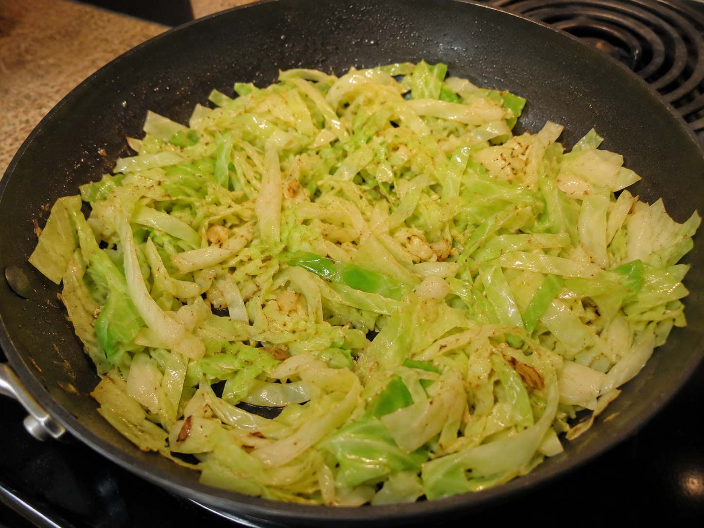 Sliced cabbage and garlic cooking in a skillet until softened.