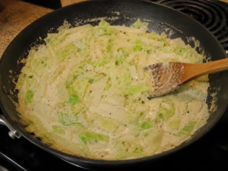 Creamy Alfredo-style sauce with cabbage, parmesan, and cream cheese cooking in a skillet.