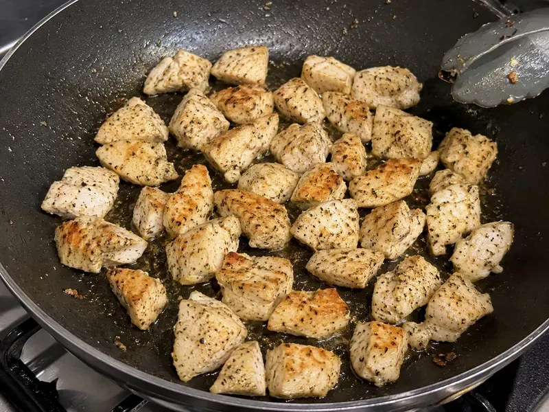 Chicken pieces cooking in a skillet until golden for creamy garlic chicken pasta.
