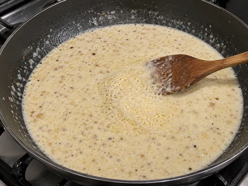 Creamy garlic Parmesan sauce cooking in a skillet with garlic, cream, broth, and cheese.