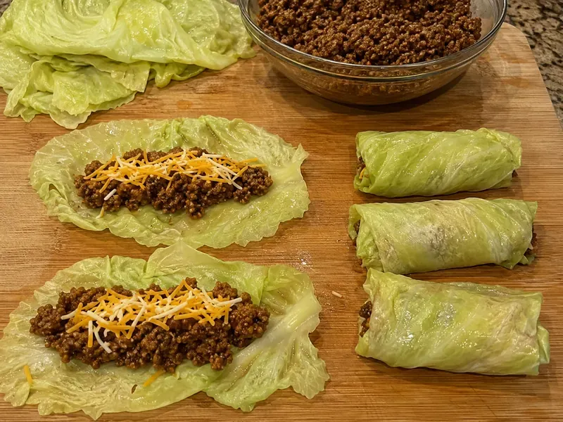 Softened cabbage leaves filled with taco beef and shredded cheese before folding.