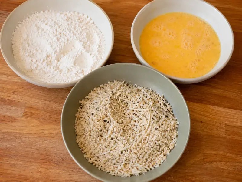 Breading station with flour, eggs, and seasoned panko for eggplant parmesan.