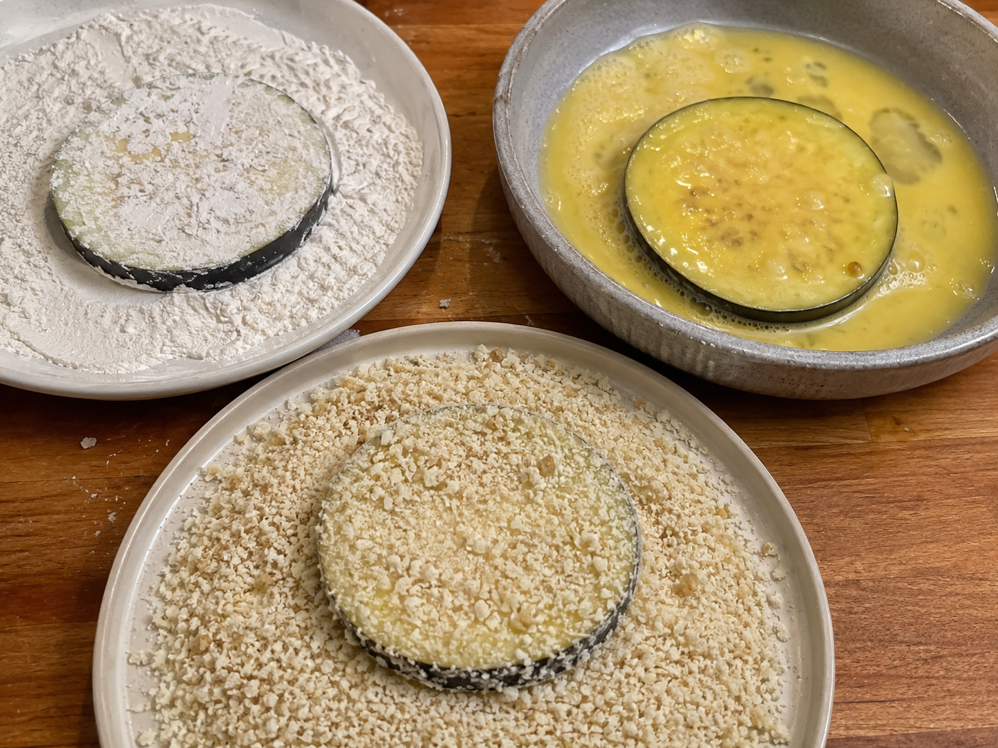 Eggplant rounds being coated in flour, egg, and breadcrumbs.