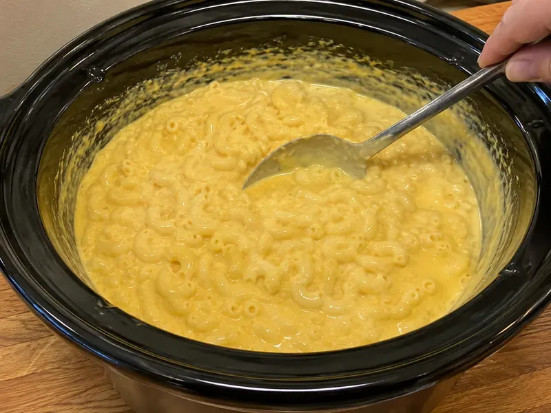 Creamy velveeta macaroni and cheese stirred with a spoon in a slow cooker.