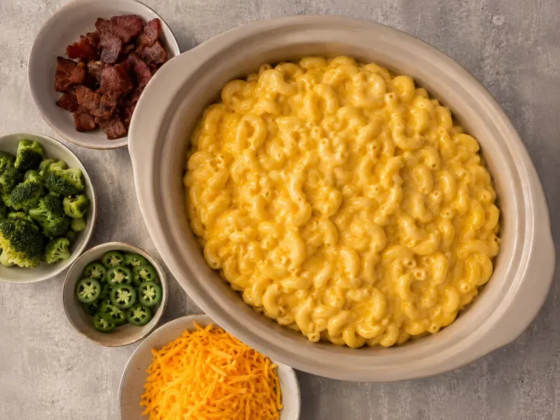 Crock Pot Recipes Mac and Cheese with Velveeta final image showing a creamy Velveeta crock pot mac and cheese base with small bowls of variation toppings like bacon, broccoli, jalapeños, and extra cheddar in a realistic potluck setup.