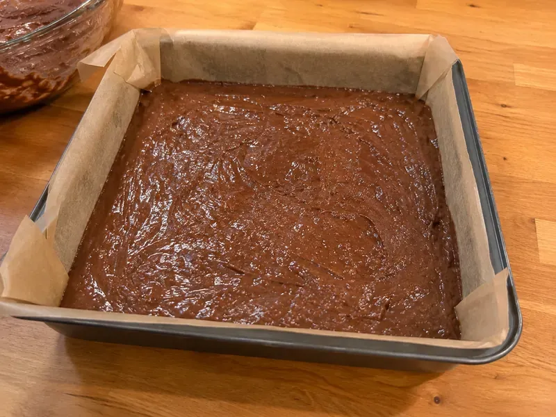 Chocolate brownie batter spread into a parchment-lined baking pan.