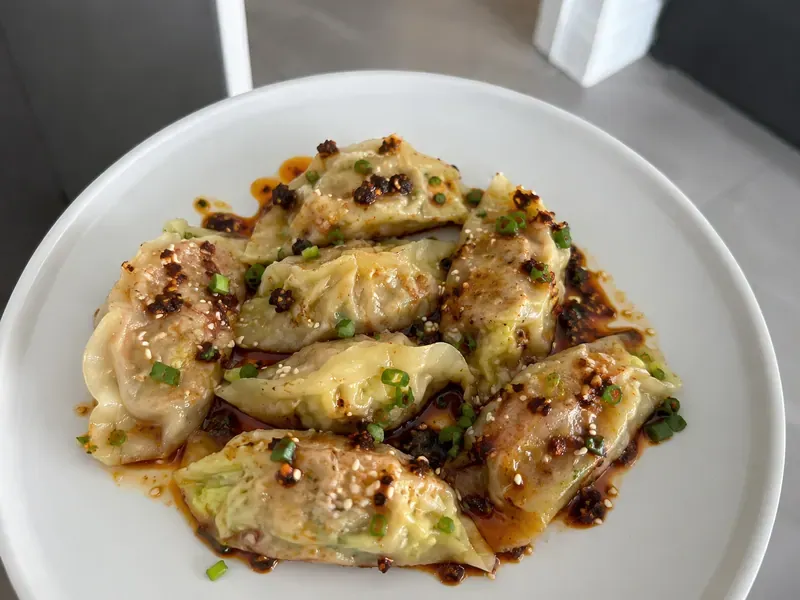 Easy cabbage dumplings with soy chili sauce, green onions, sesame seeds, and chili crisp.