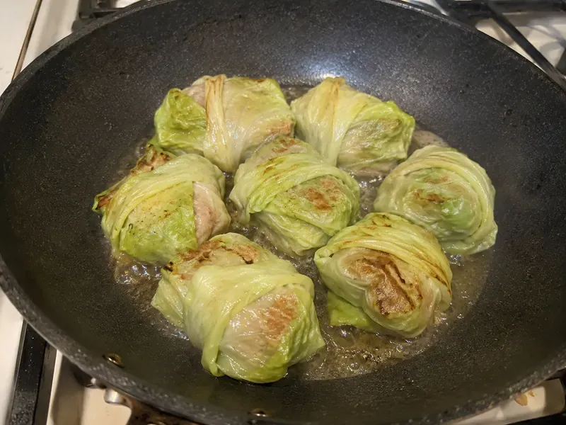 Cabbage dumplings steaming and crisping in a skillet.
