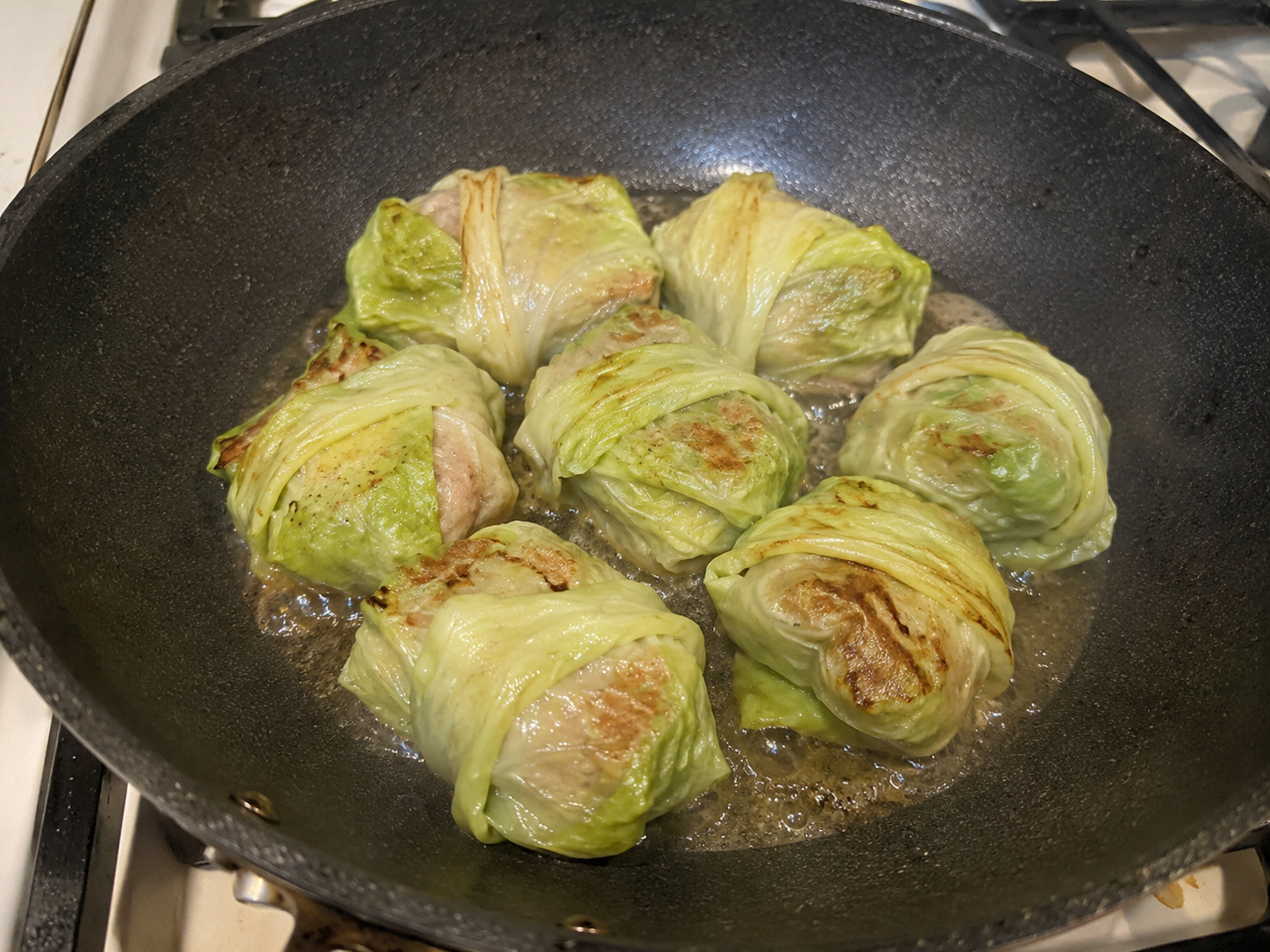 Cabbage dumplings steaming and crisping in a skillet.