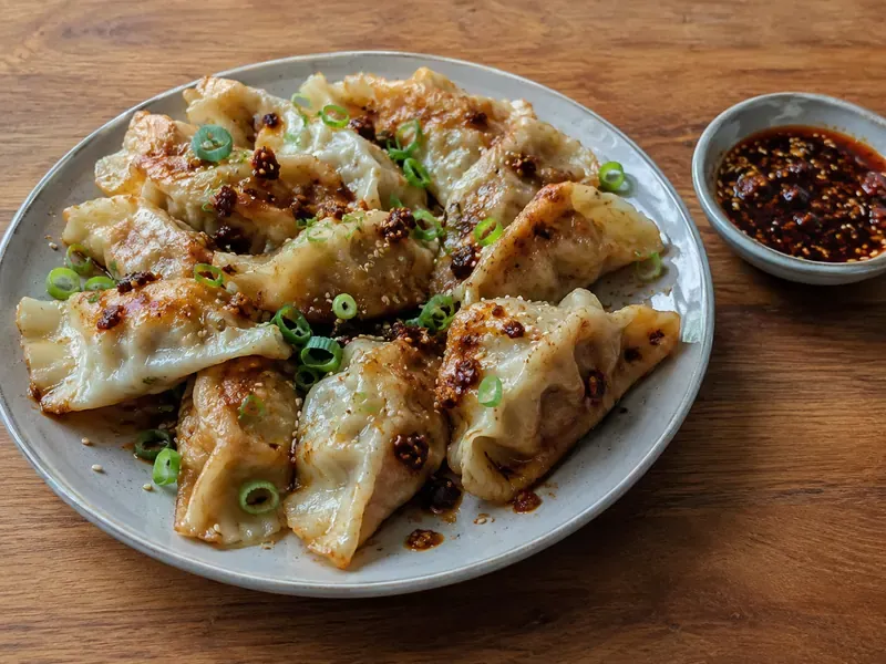 Finished cabbage dumplings served with soy chili sauce, green onions, sesame seeds, and chili crisp.