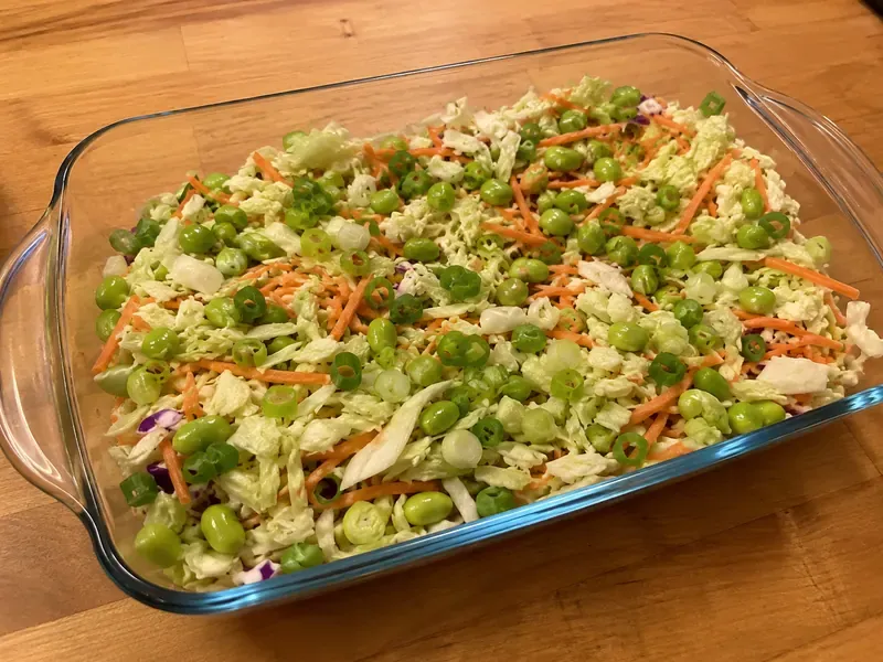 Baking dish filled with cabbage, edamame, carrots, and green onions for frozen dumpling bake.