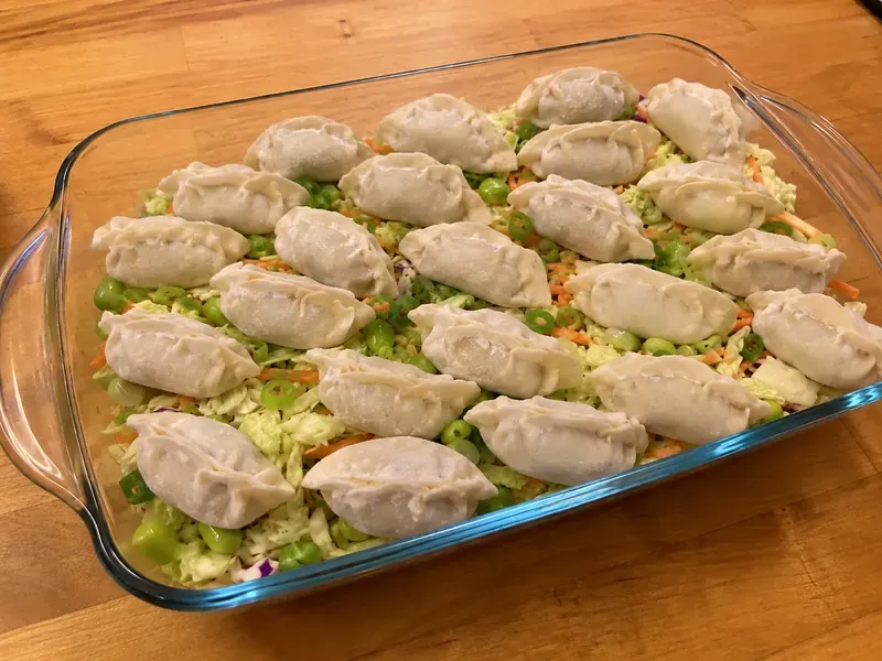 Frozen dumplings arranged over cabbage, carrots, and edamame in a baking dish.