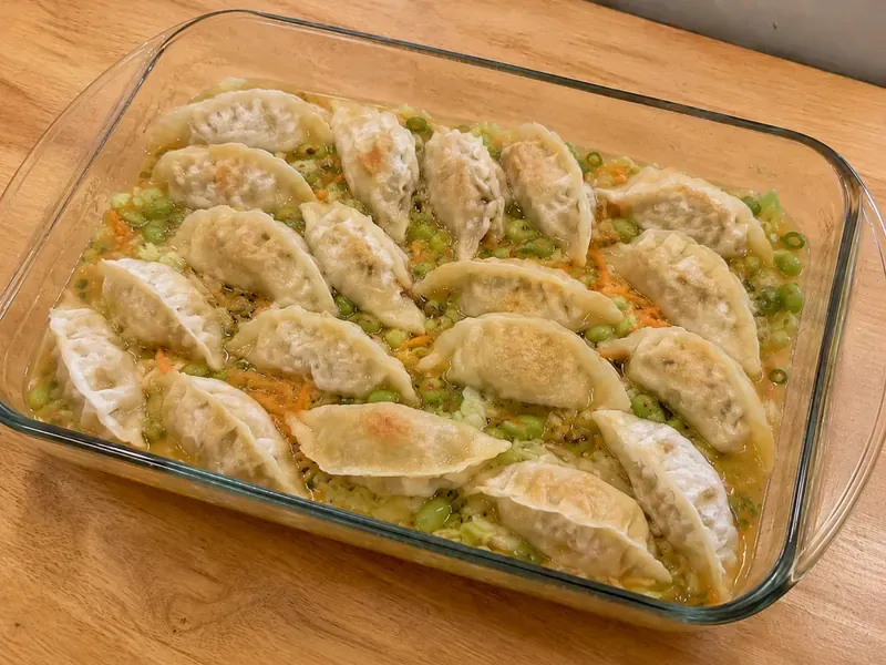 Baked frozen dumplings with cabbage, carrots, edamame, and saucy broth in a baking dish.
