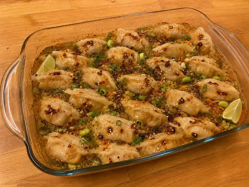 Finished frozen dumpling bake with chili crisp, green onions, sesame seeds, cabbage, carrots, and edamame.