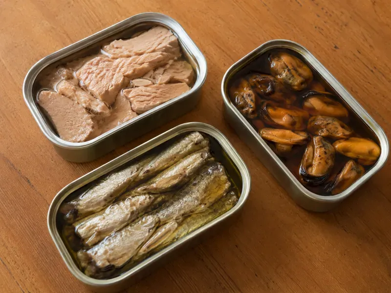 Opened tins of sardines, tuna, and smoked fish for a tinned fish board.