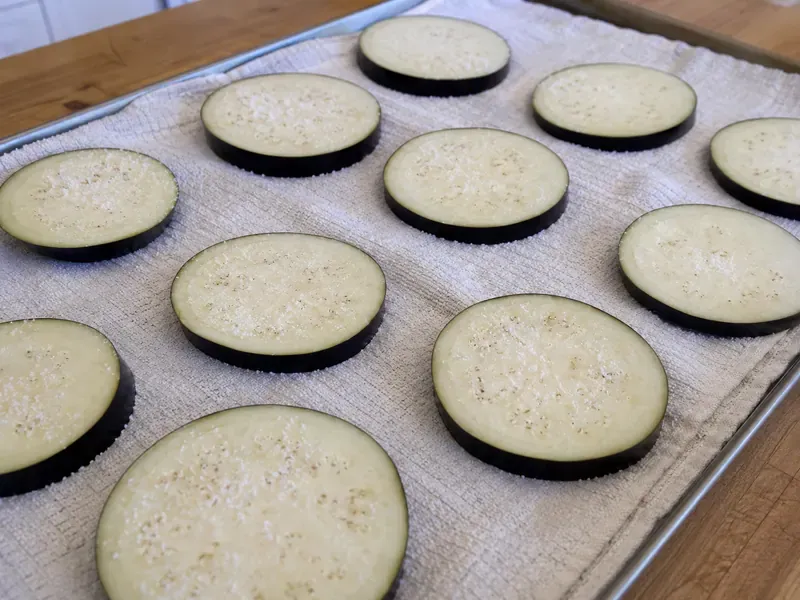 Eggplant slices salted on a towel or baking sheet.