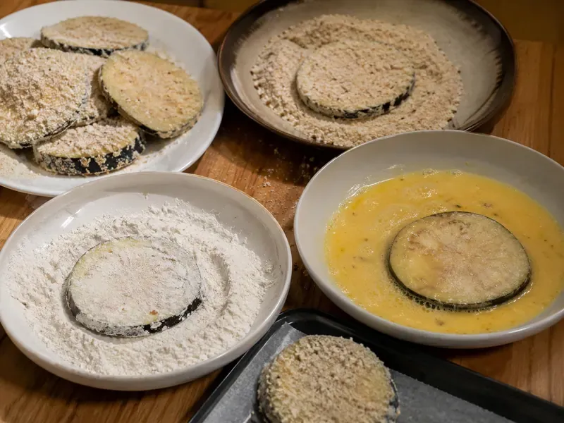 Eggplant slices coated in flour, egg, and breadcrumb mixture.