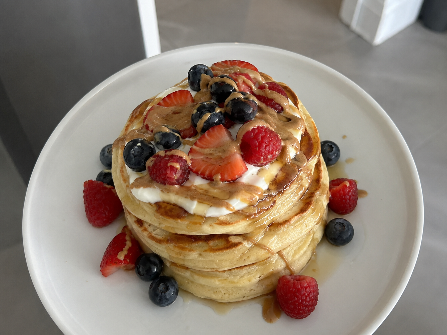 Fluffy cottage cheese protein pancakes with berries, Greek yogurt, maple syrup, and nut butter drizzle.