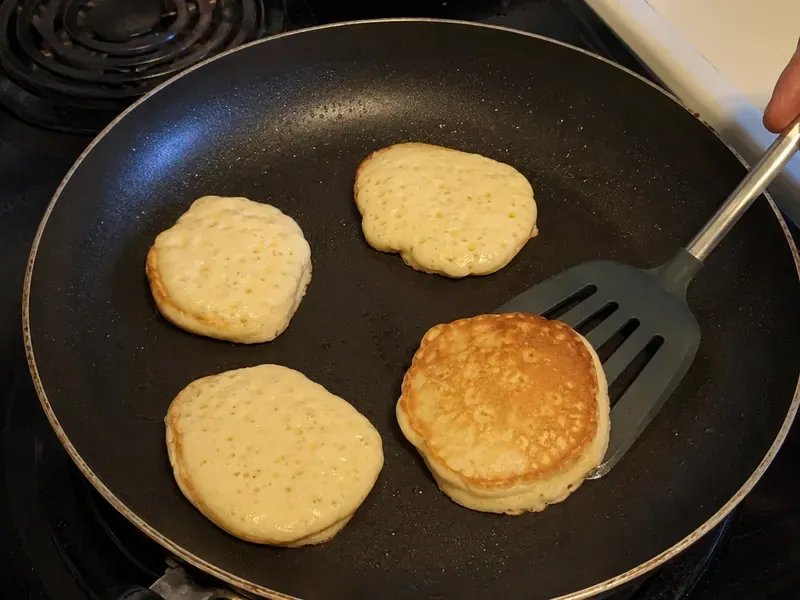 Small cottage cheese protein pancakes cooking in a skillet with bubbles and lightly set edges.