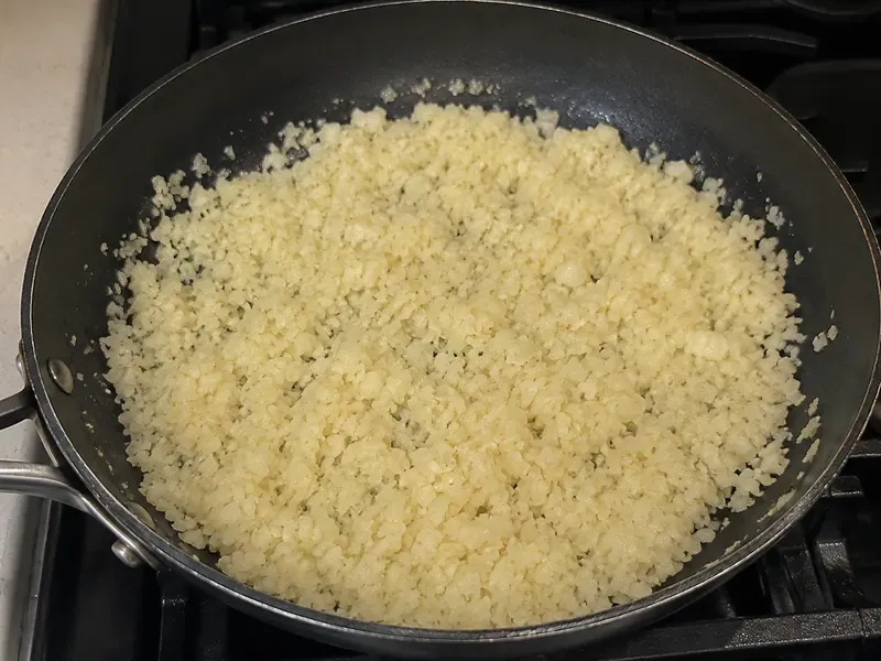 Cauliflower rice cooking in a skillet with olive oil and salt.