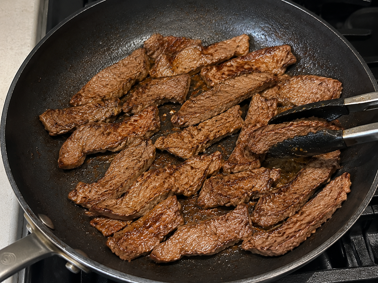 Thin slices of lean beef searing in a skillet until browned.