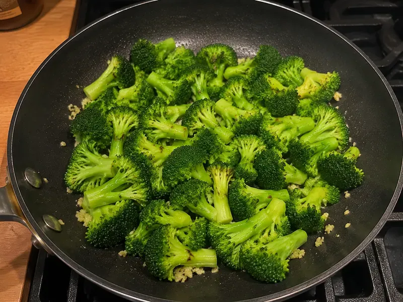 Broccoli florets cooking with minced garlic in a skillet.