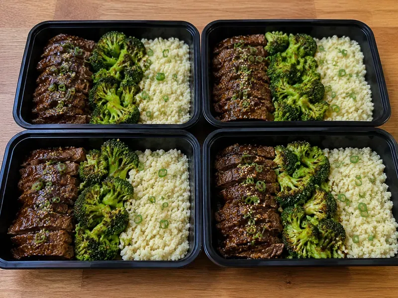 Finished garlic beef and broccoli meal prep boxes with cauliflower rice, beef slices, broccoli, and garlic sauce.